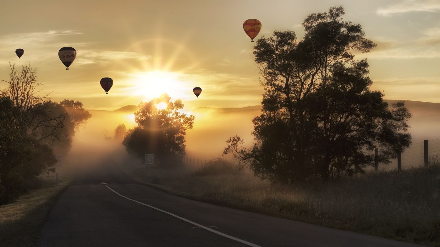 Des montgolfières en silhouette au-dessus d’une campagne brumeuse, au lever du soleil
