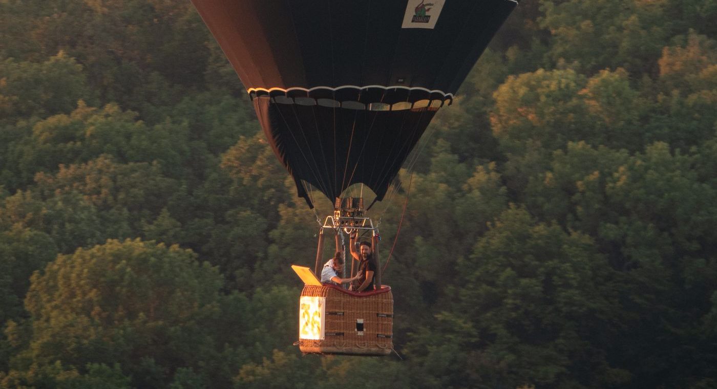 Deux passagers dans une petite nacelle, au ras d’une forêt, au soleil couchant