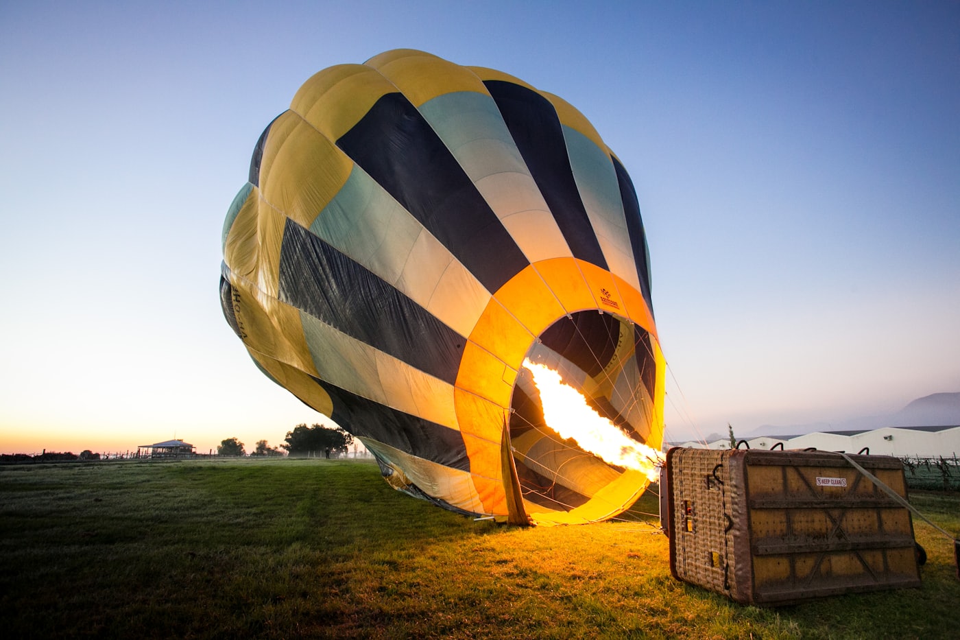 Une montgolfière en cours de gonflage au sol, brûleur allumé, à l’aube