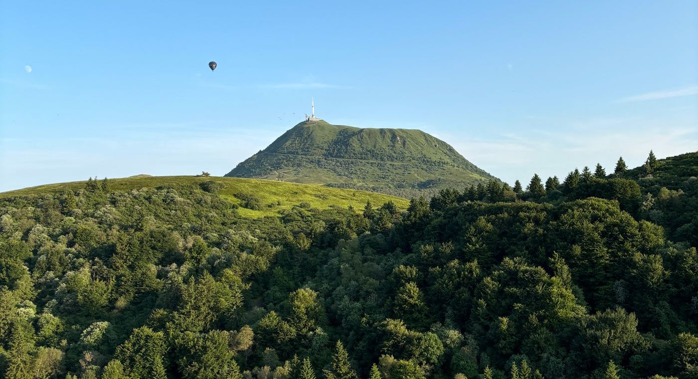 Une montgolfière passant à côté du Puy de Dôme, plus bas que le sommet, au-dessus de forêts