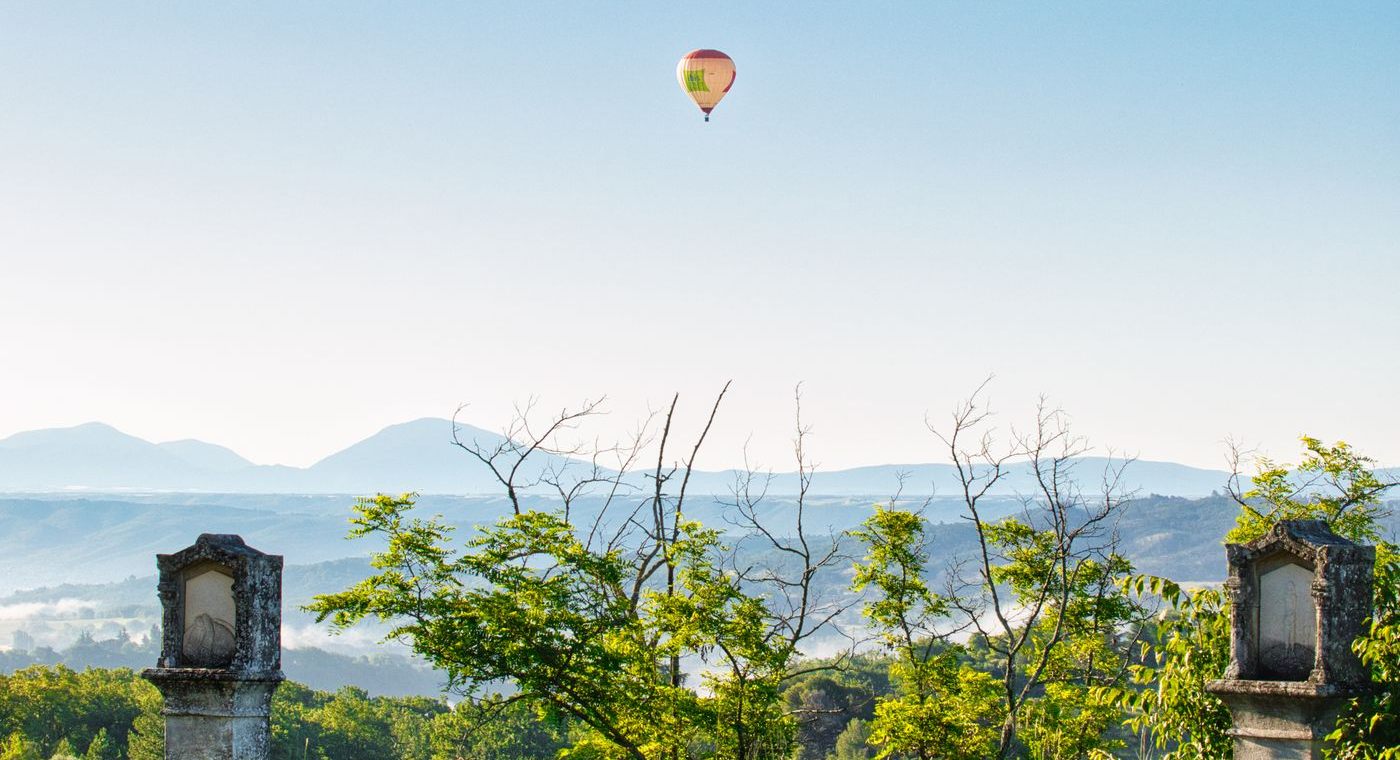 Une montgolfière au loin, vue depuis une terrasse à balustres, brume dans la vallée