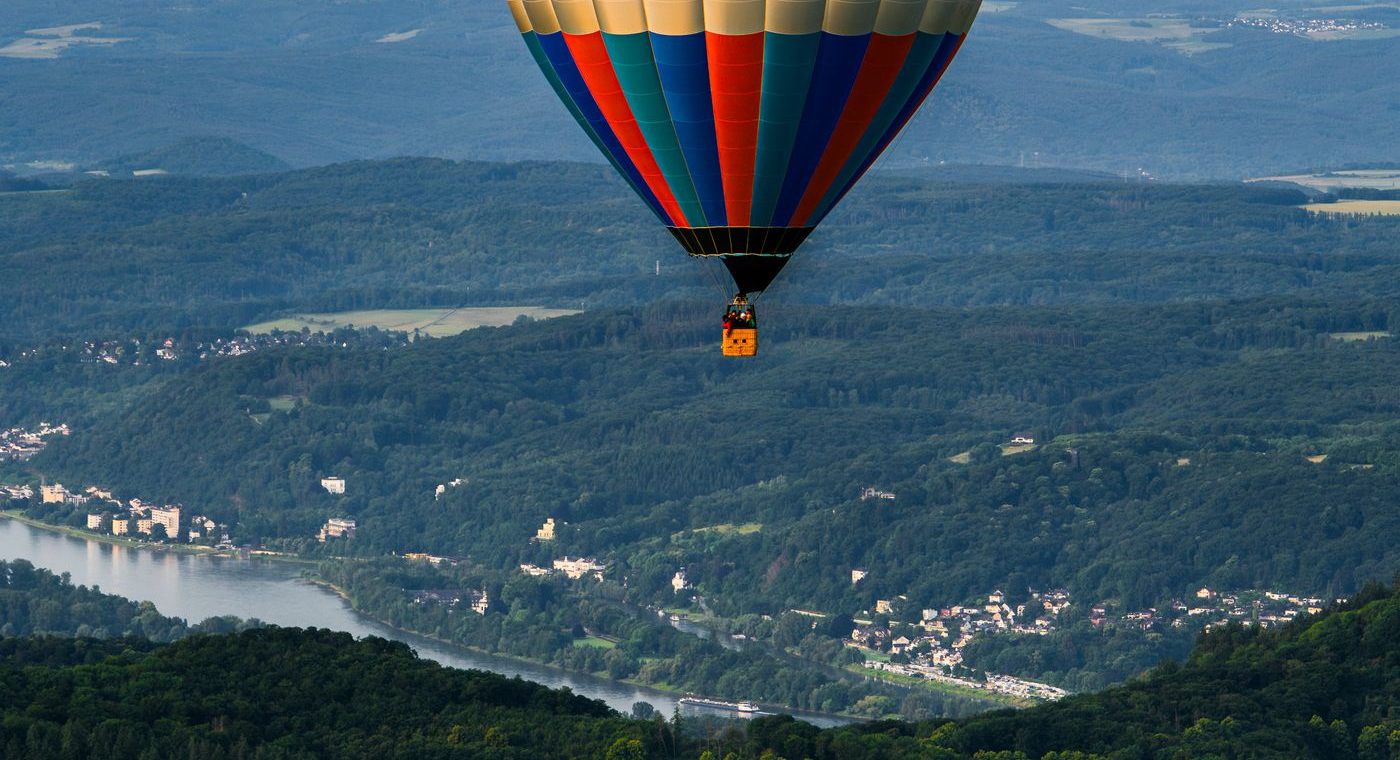 Une montgolfière au-dessus d’une vallée fluviale boisée, une péniche sur la rivière en contrebas