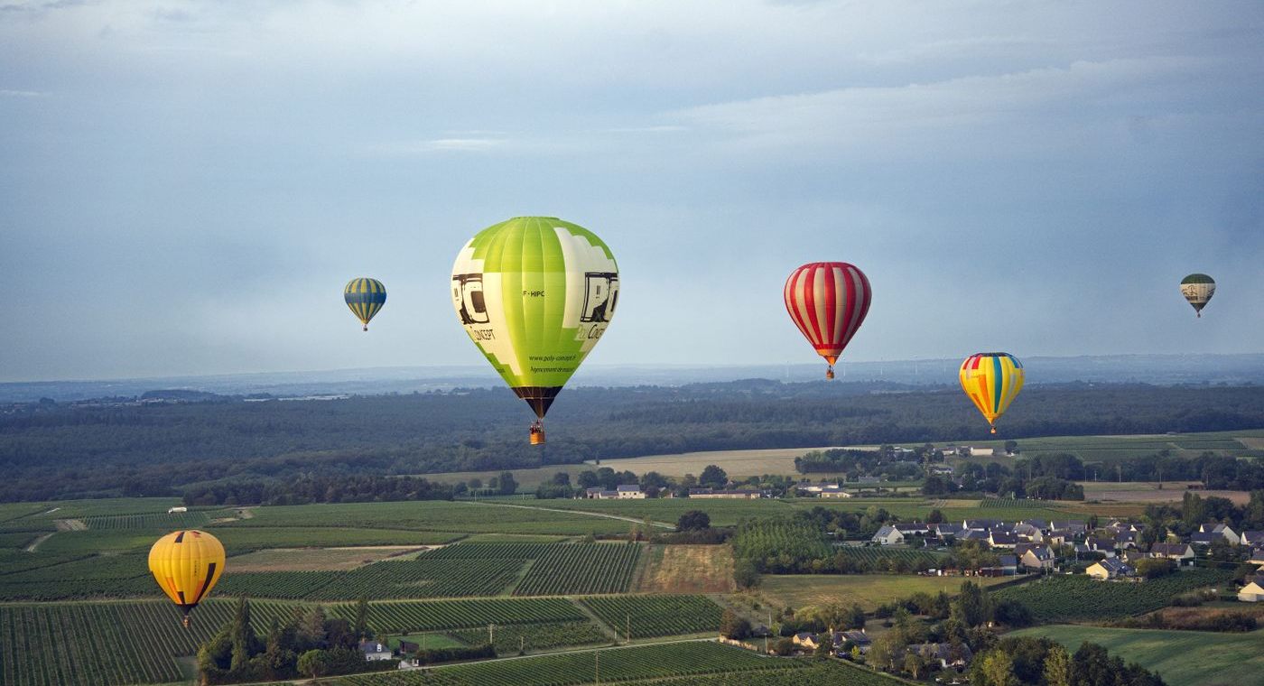 Six montgolfières au-dessus d’un damier de vignes et de villages, à l’aube